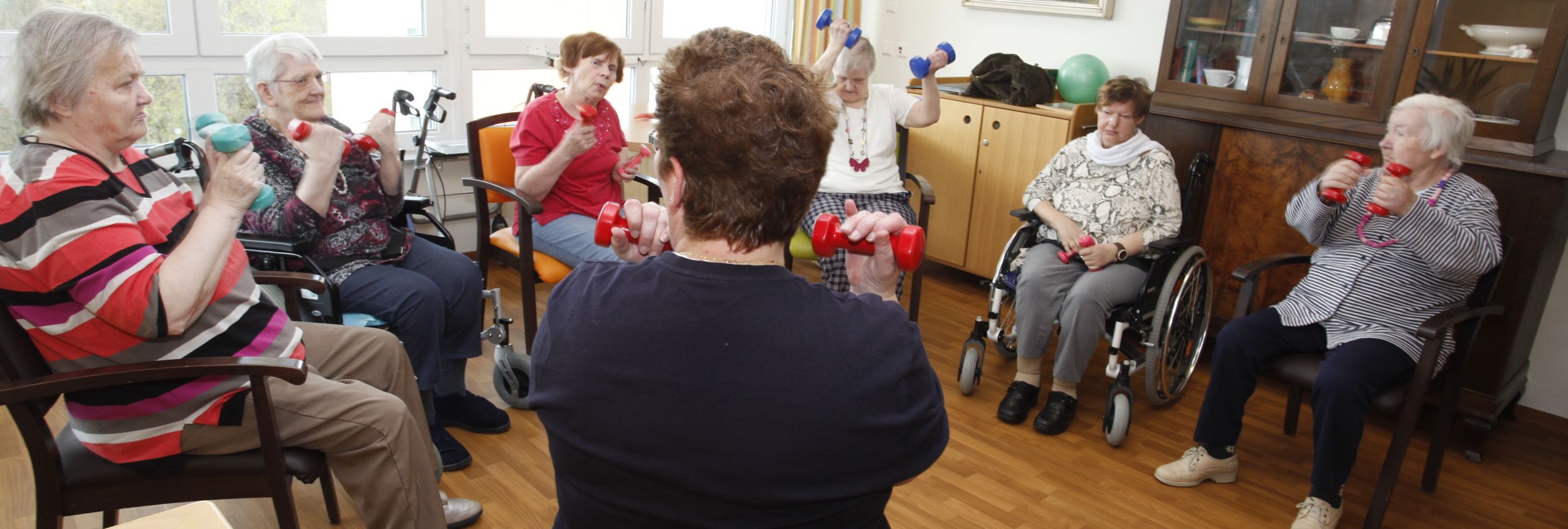 Sitzende Seniorinnen im Kreis machen Übungen mit Kurzhanteln