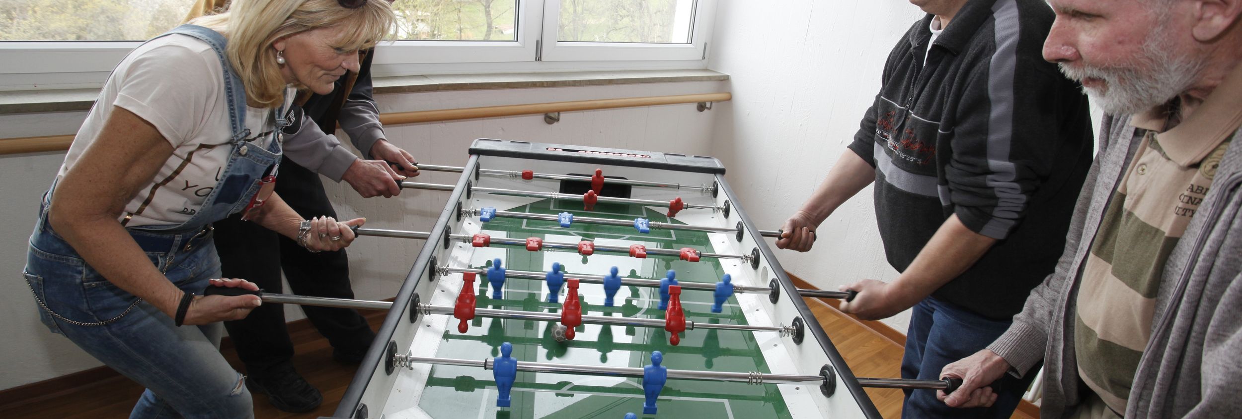 Vier Erwachsene spielen Tischkicker an einem Fenster